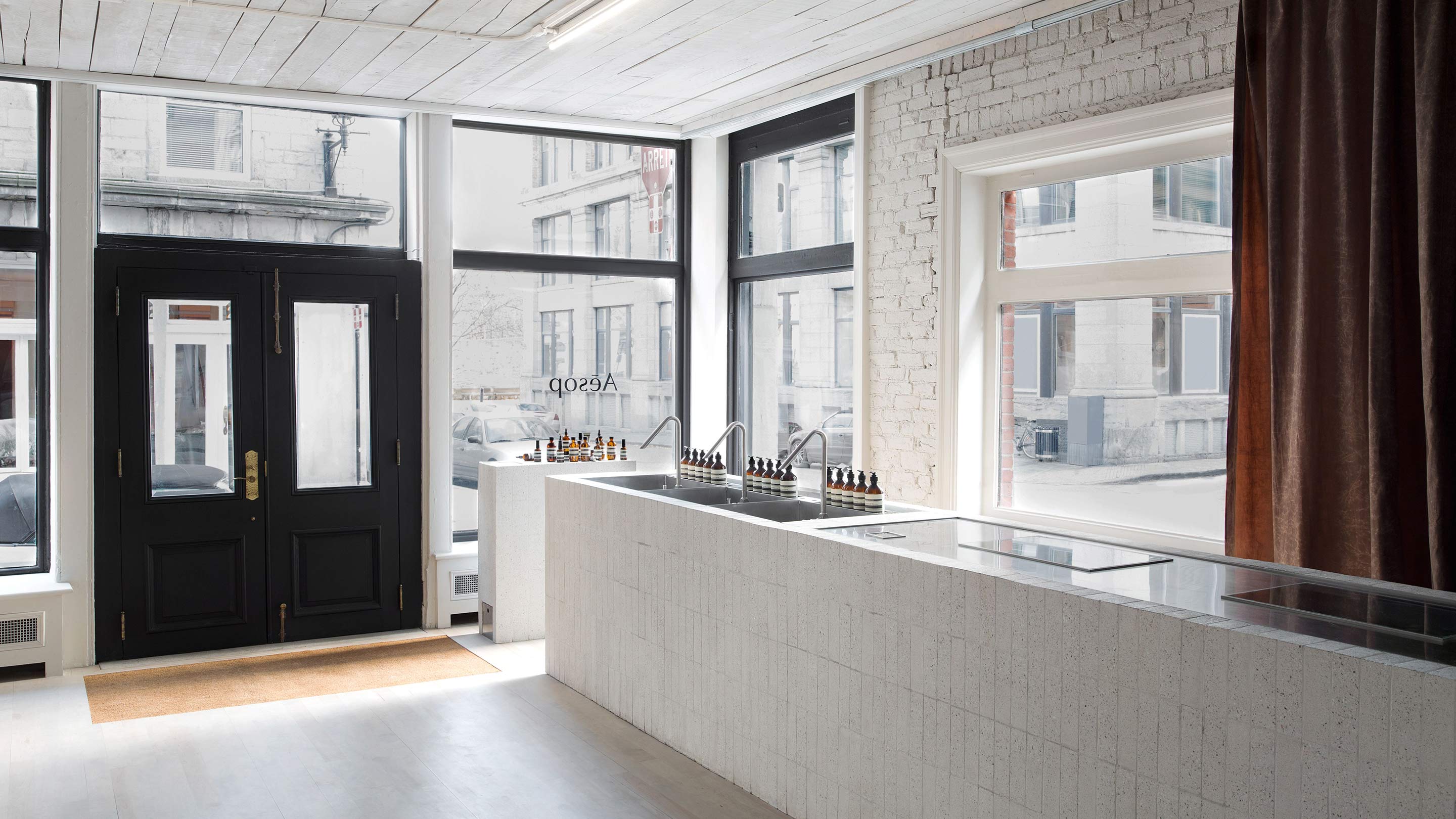An industrial-style store space featuring a white, brick sink and counter; sitting in front of large windows.