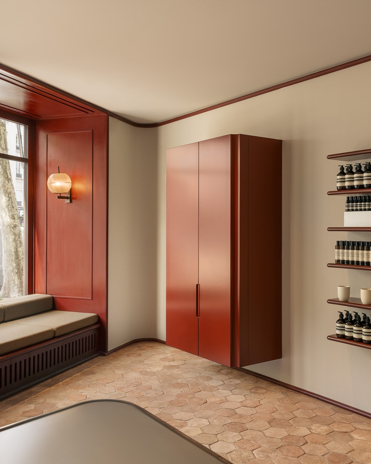 Aesop Avenue des Ternes store interior with hexagonal tiles, window bench seating and deep red fragrance armoire.
