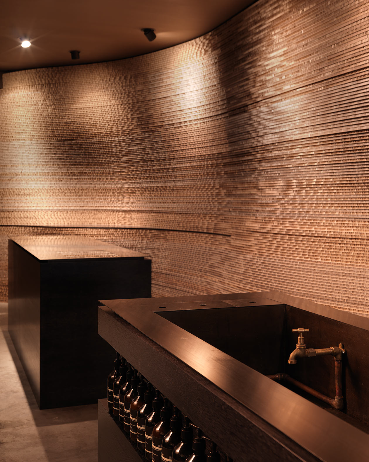 A dark customer experience basin, made with dark timber and dark, brass fixtures.