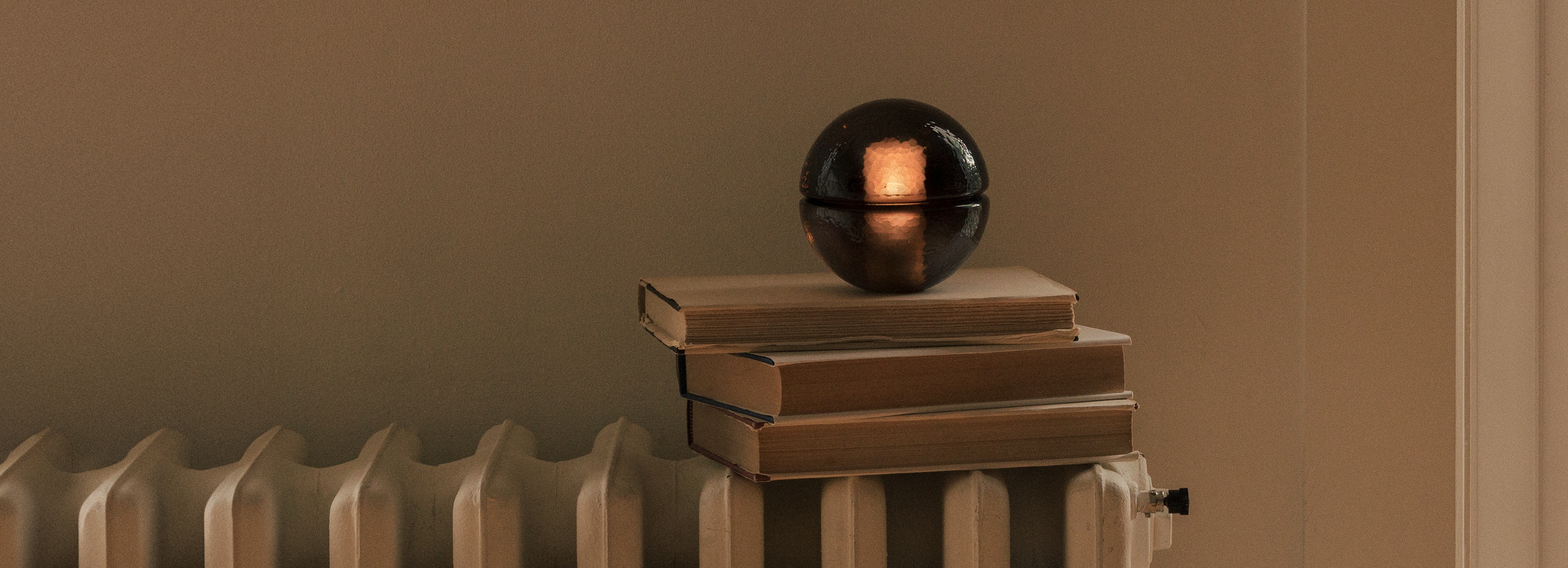 orb-shaped amber glass Bocci 14p lamp illuminated, sitting atop stack of three hardcover books on a radiator