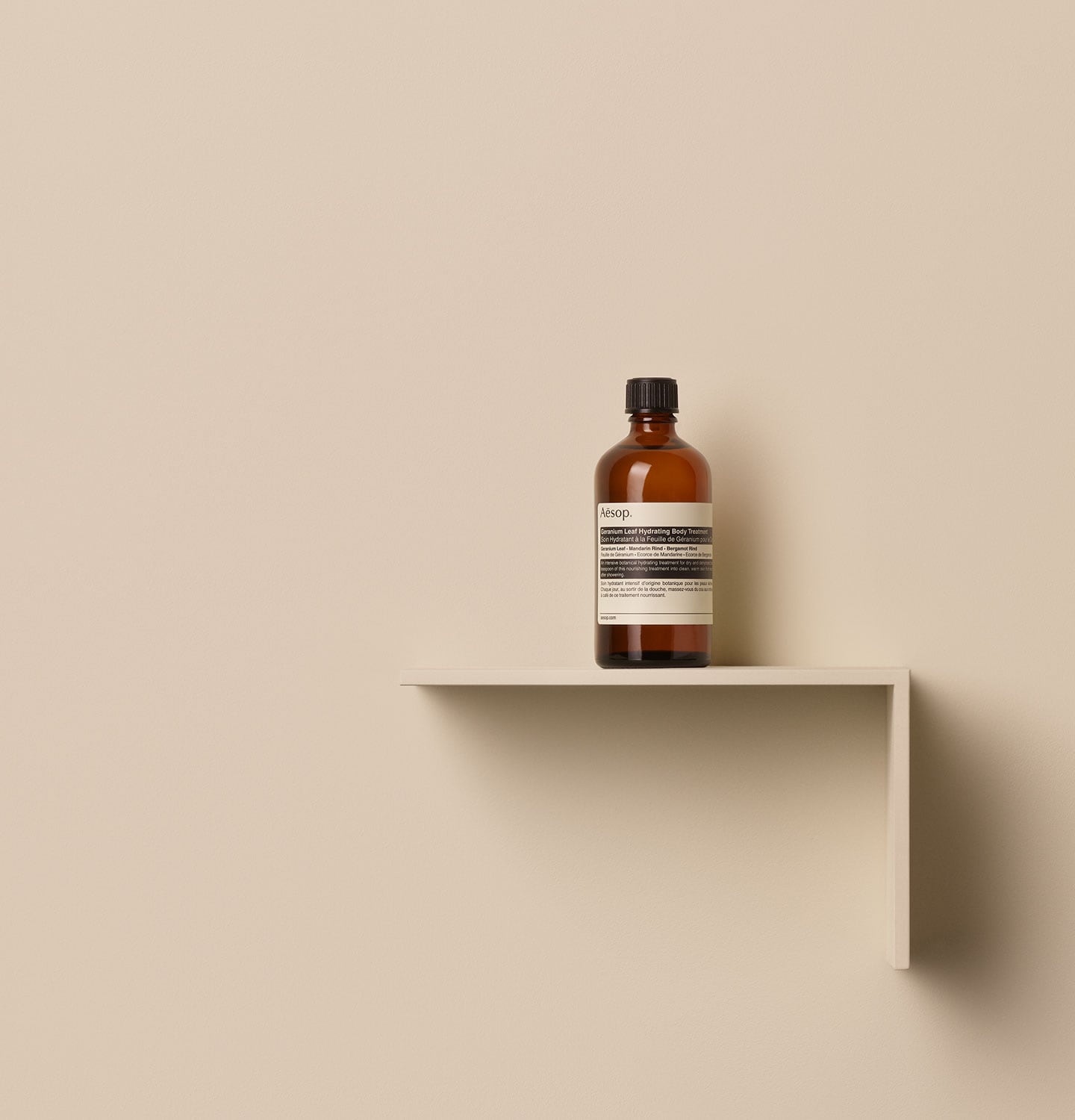Aesop Geranium Leaf Hydrating Body Treatment in glass amber bottle, placed on a shelf in a beige background
