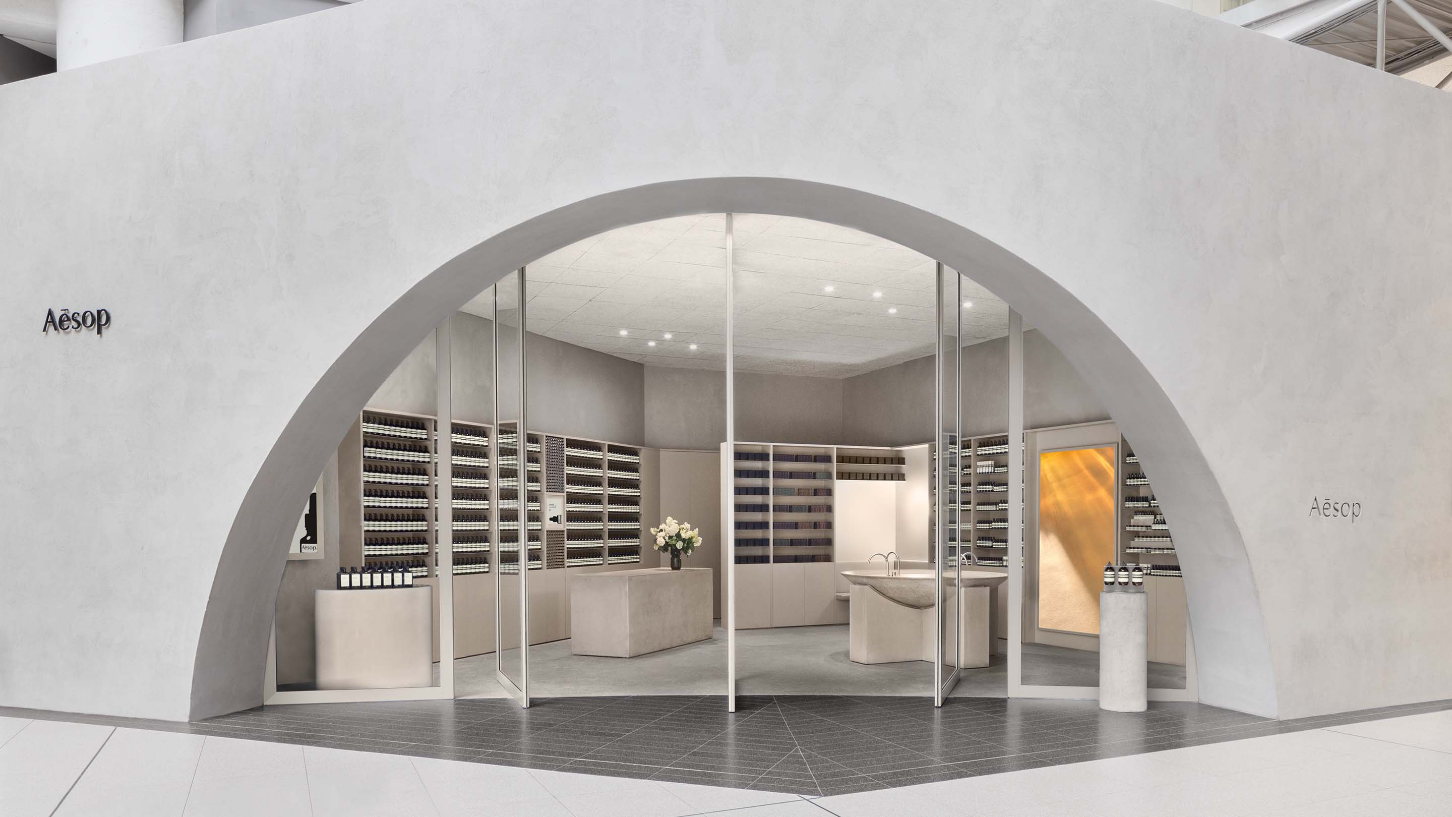 Front entrance to Aesop Toronto Eaton Centre comprising of large glass doors beneath a stone curved opening.
