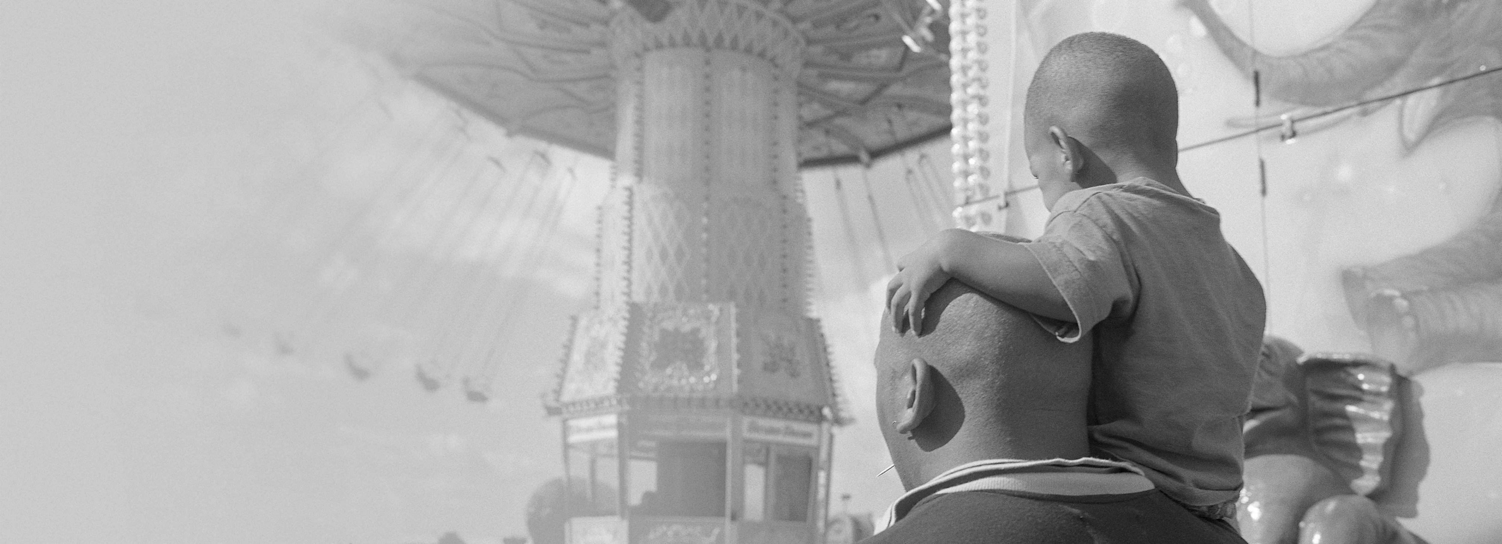 An adult carrying a kid next a ride at theme park