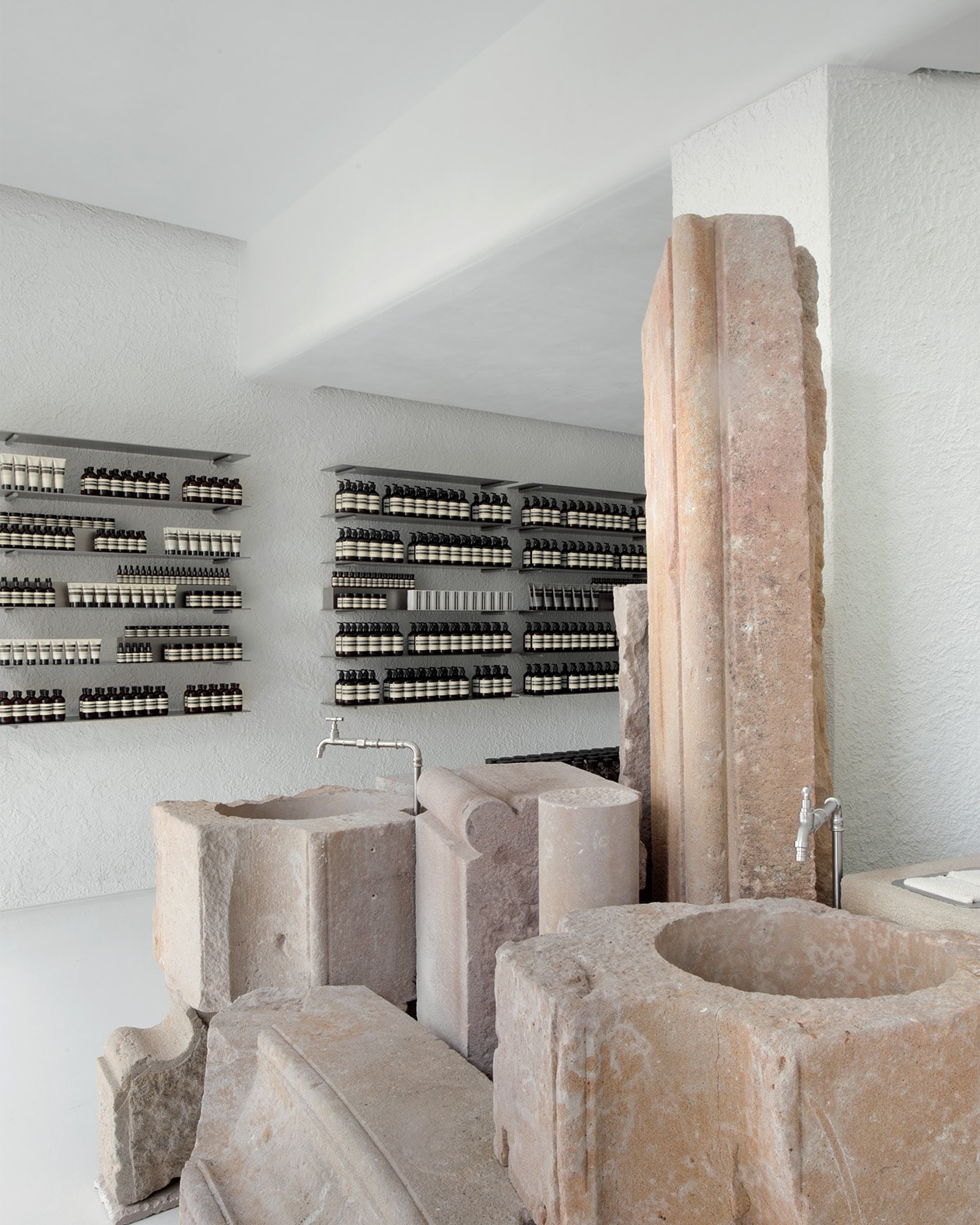 Aesop Diagonal store interior, carved stone basin and amber bottle product display on metal shelving units.