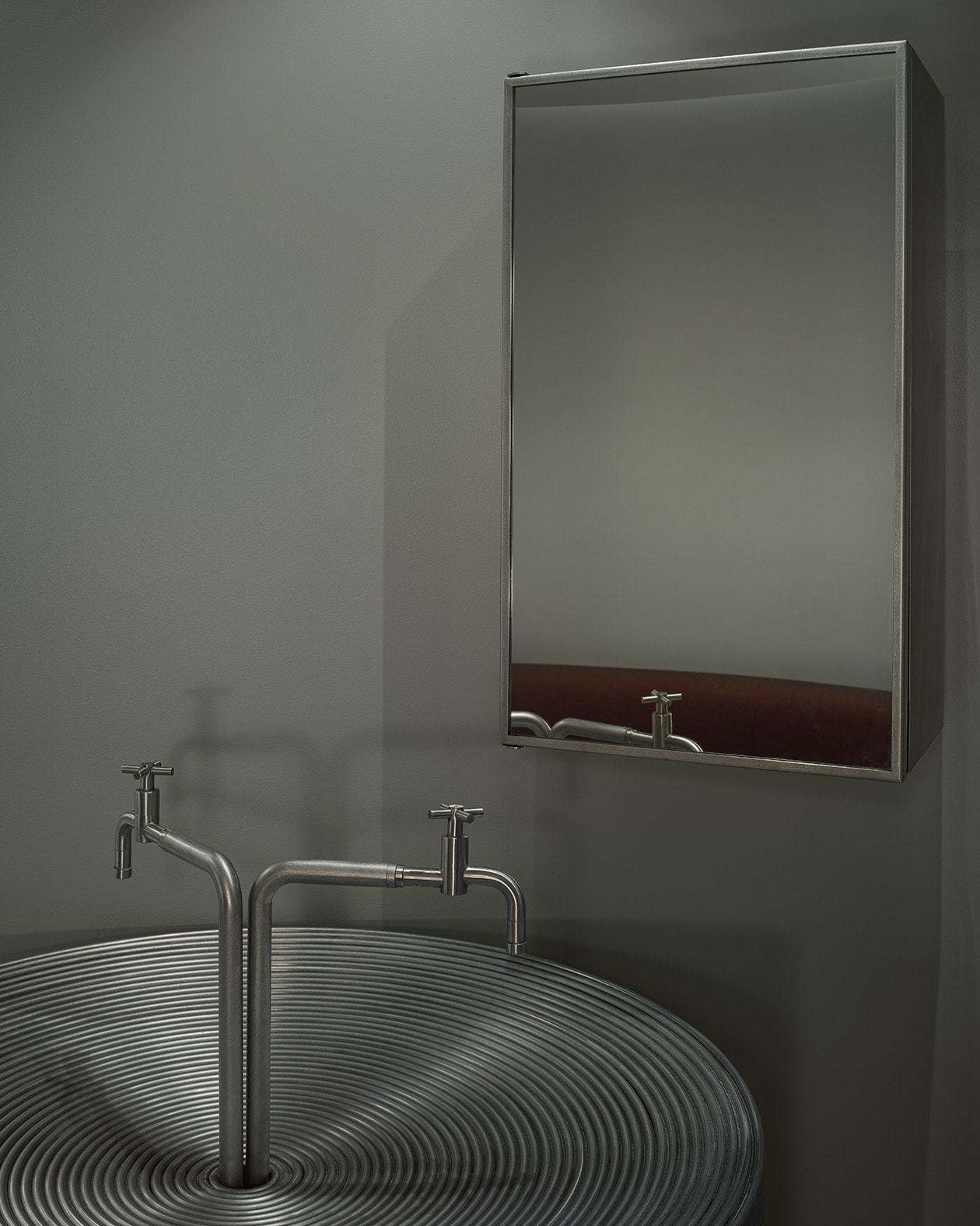 photo of mirror with steel frame on grey wall above dual spouted faucet and ridged sink