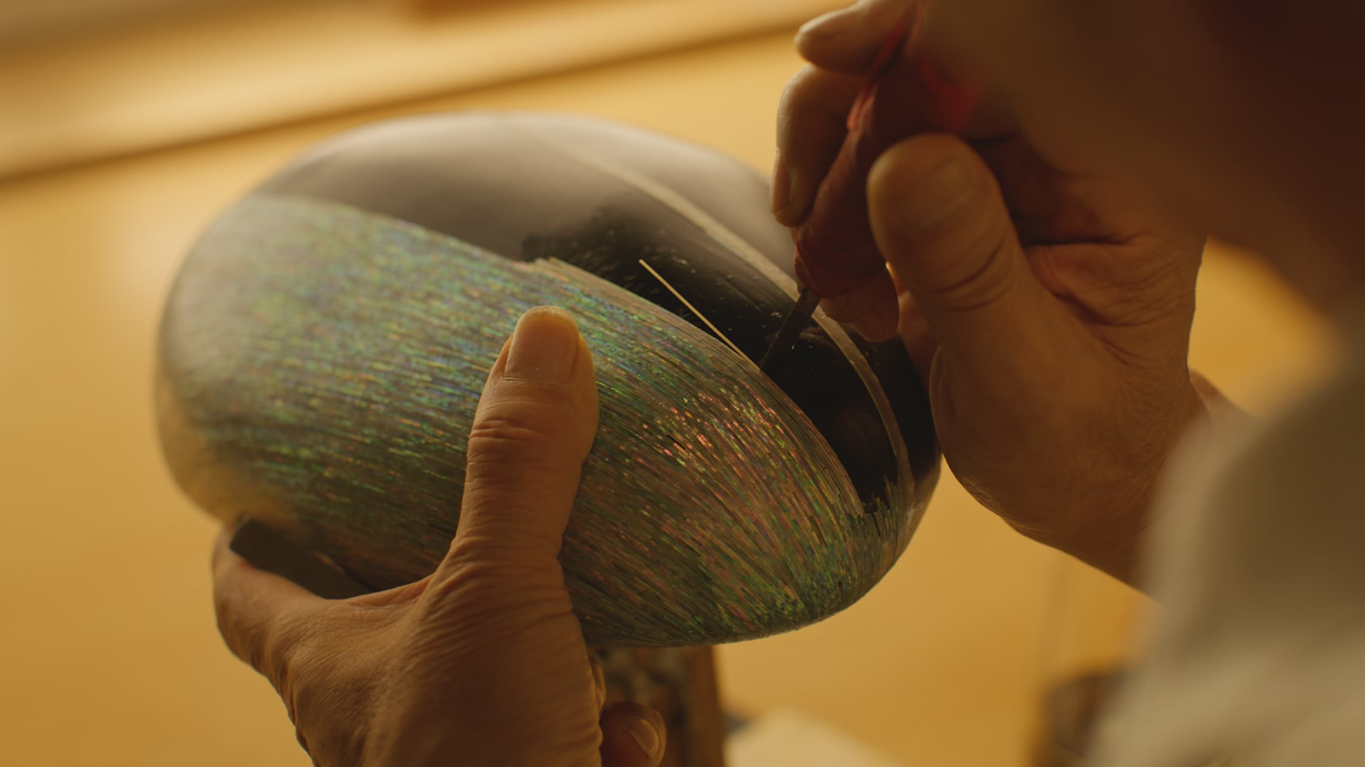 A man holding a small carving tool carving an iridescent surface made of mother-of-pearl.