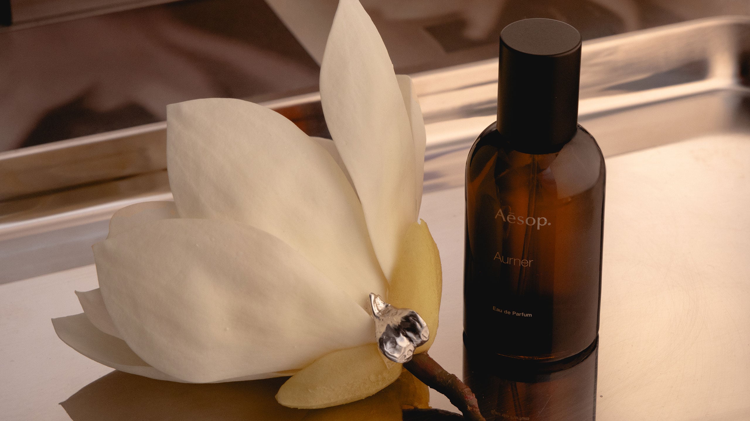 A silver ear cuff, magnoilia flower and Aurner EDP bottle placed on a metal tray