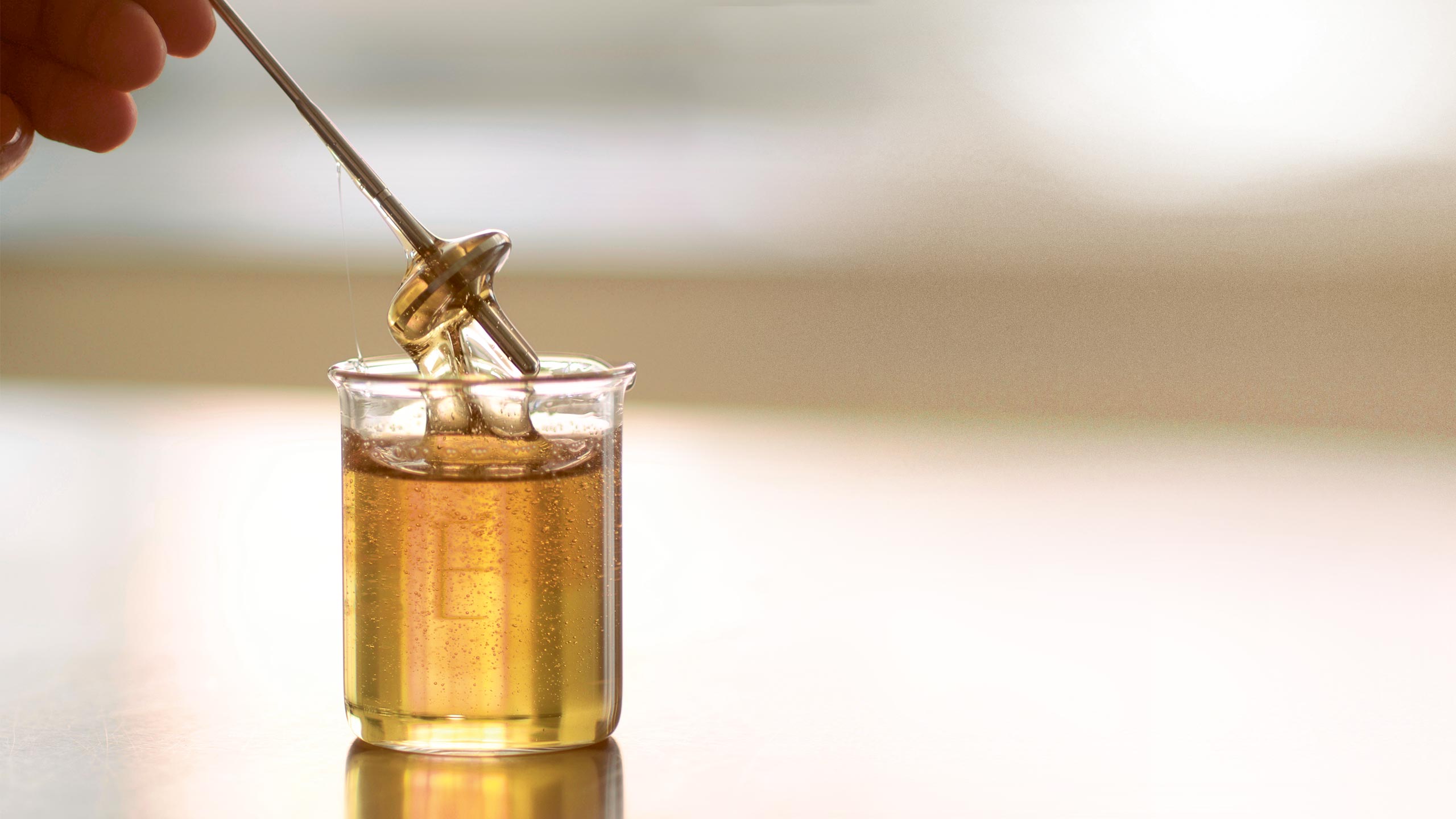 Close-up of glass beaker filled with viscous, honey-like solution in which a metal tester is partially submerged.