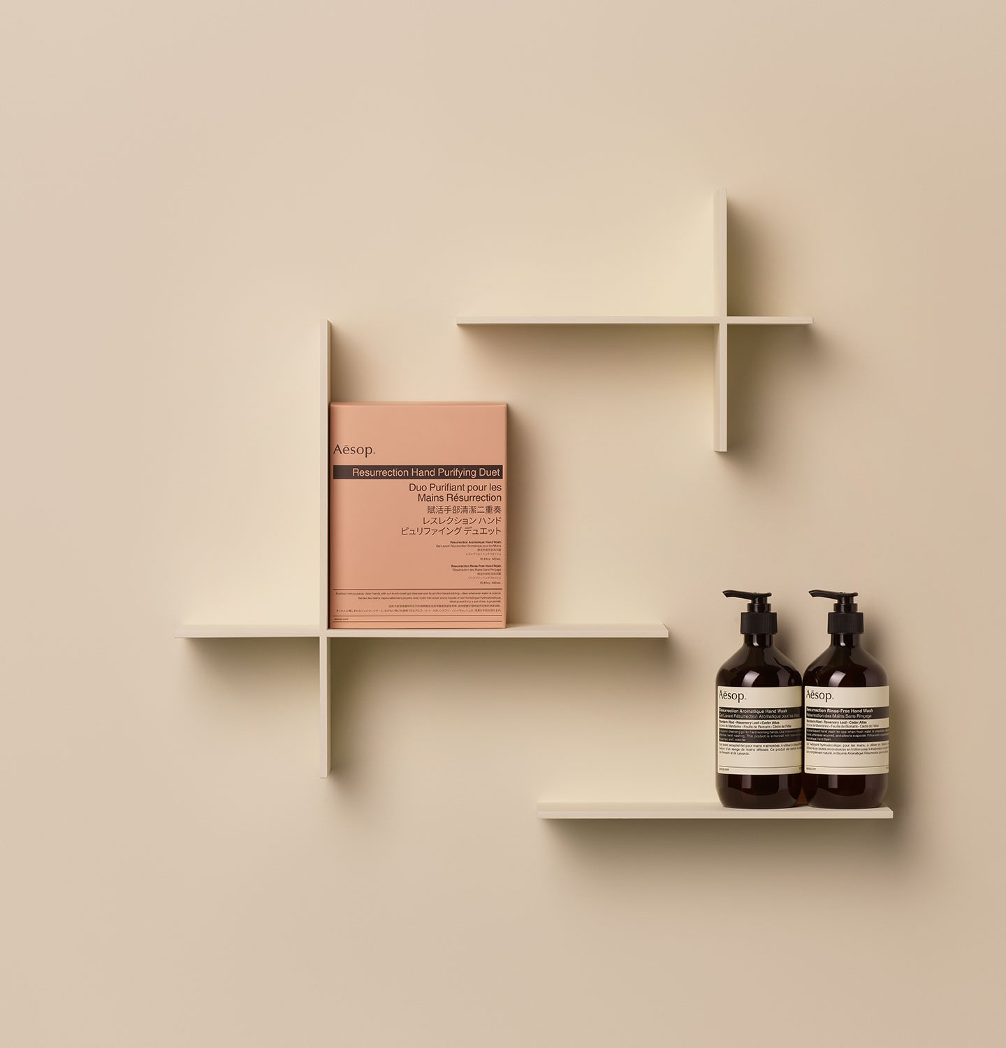 Aesop Resurrection Hand Purifying Duet paper packaging and amber pump bottles arranged on a wooden object in a beige background